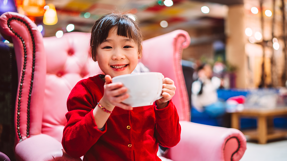 Lovely cheerful girl smiling joyfully at the camera while drinking a cup of hot chocolate in cafe.